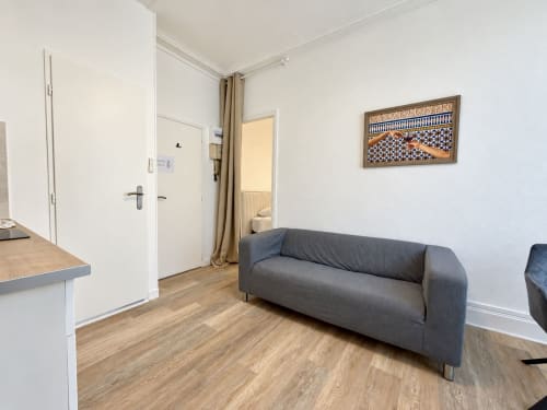 Spacieuse chambre moderne à l'hôtel Nancy-Place avec canapé gris, murs blancs, parquet et décoration contemporaine