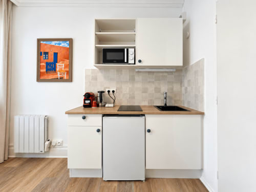 Kitchenette compacte à l'hôtel NANCY-PLACE avec placards crème, plan de travail en bois, micro-ondes et art mural coloré à Nancy