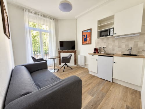 Studio moderne à l'hôtel Nancy-Place avec canapé gris, kitchenette, TV et accès au balcon à Nancy