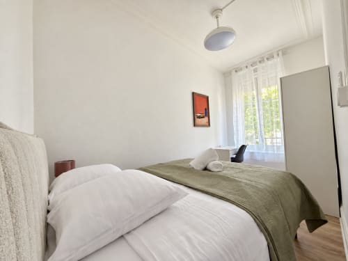 Chambre lumineuse à l'hôtel Nancy-Place avec oreillers blancs, literie verte, parquet et grande fenêtre aux voilages