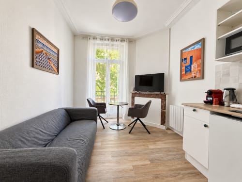 Studio moderne à l'hôtel Nancy-Place avec canapé gris, kitchenette, TV et balcon vue sur la ville