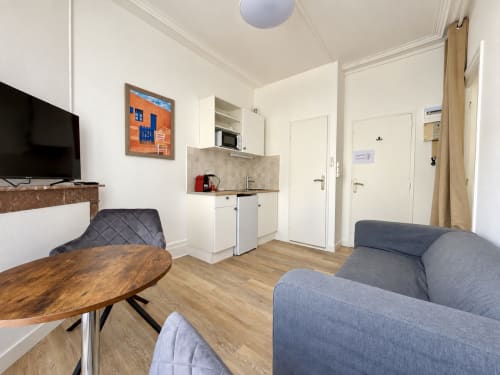 Studio compact à l'hôtel NANCY-PLACE avec kitchenette, TV, table en bois et assises grises à Nancy