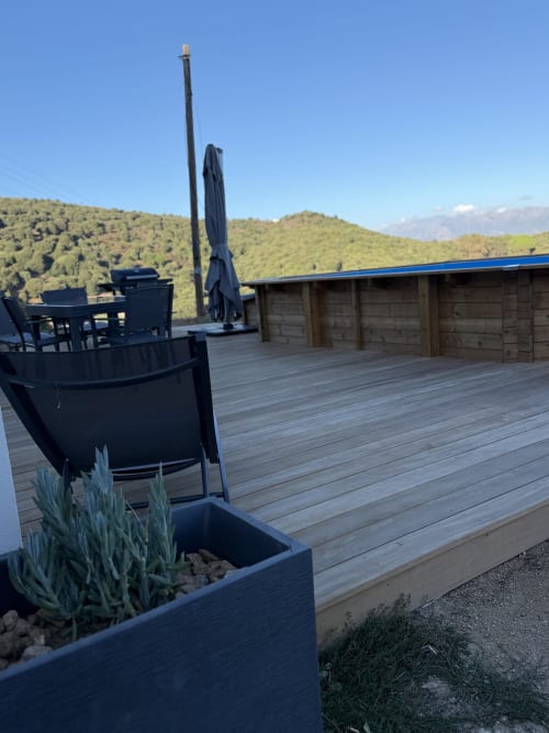 Terrasse en bois avec parasol bleu et mobilier au Petit Coin de Paradis B&B à Alata, entourée de collines verdoyantes