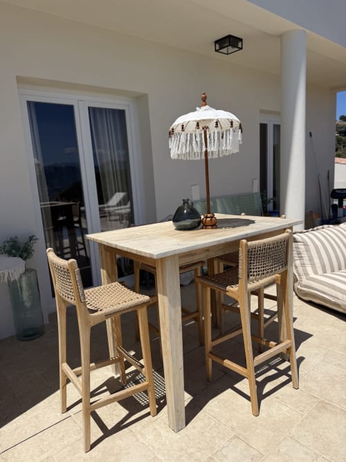 Terrasse extérieure du Petit Coin de Paradis BnB à Alata avec table de bar, chaises tressées et parasol blanc à franges