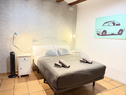 Dormitorio moderno en apartamento de Valencia con cama blanca, iluminación contemporánea y cuadro de auto vintage en pared turquesa