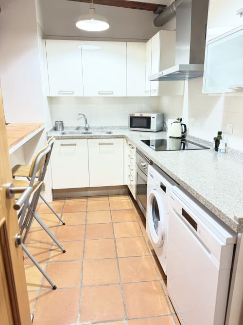 Cocina moderna con muebles blancos, encimeras de granito, lavadora y estufa en apartamento urbano Bisbe Colón, Valencia