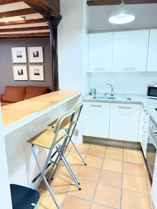 Cocina y comedor moderno en apartamento de Valencia con muebles blancos, barra de madera y suelo de baldosa terracota