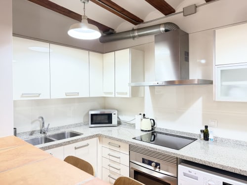Cocina moderna del Apartamento Urbano Bisbe Colón, València, con muebles blancos, encimeras de granito y electrodomésticos de acero inoxidable