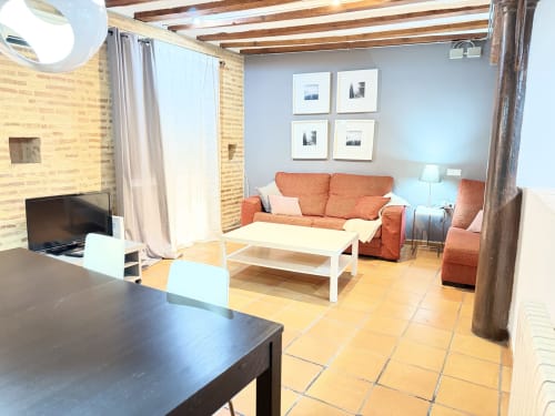 Amplio salón de apartamento en Valencia con paredes de ladrillo, sofá naranja, mesa de comedor y comodidades modernas