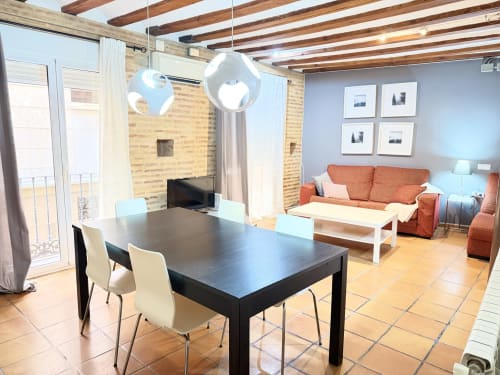 Moderno apartamento en Valencia con mesa de comedor, sofá naranja, paredes de ladrillo visto y vigas de madera - Apartamento Urban Bisbe Colón