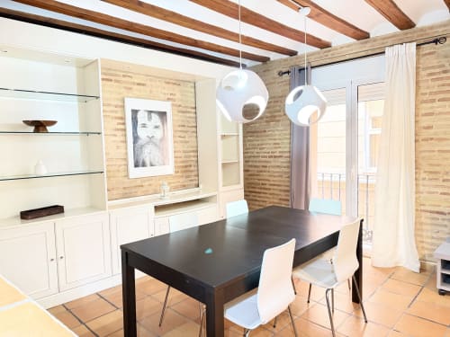 Comedor moderno en Apartamento Urban Bisbe Colón, València, con mesa negra, sillas blancas, paredes de ladrillo visto y lámparas colgantes