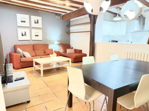 Sala de estar y comedor de apartamento moderno en Valencia con sofá naranja, vigas de madera, cocina y vistas a la ciudad en Stay Gest