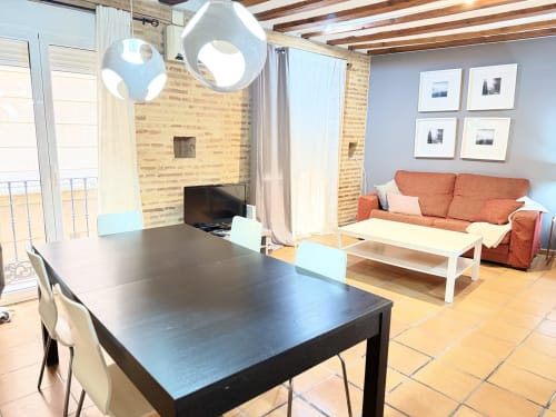 Moderno apartamento en Valencia con salón, mesa de comedor, sofá naranja, paredes de ladrillo y vistas a la ciudad desde el balcón