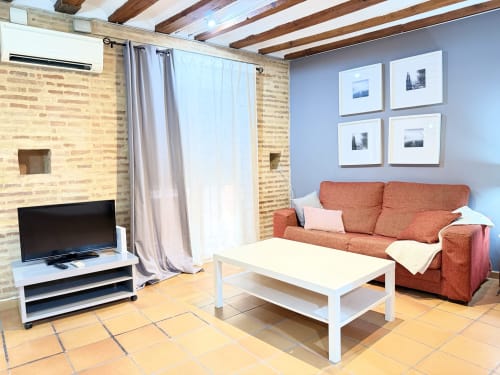 Luminoso salón de apartamento moderno en Valencia con sofá terracota, mesa de café blanca, televisor y paredes de ladrillo visto