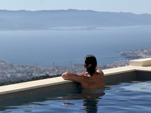 Invité se relaxant dans une piscine à débordement avec vue sur la ville côtière d'Alata et la mer Méditerranée à l'hôtel boutique Petit Coin de Paradis