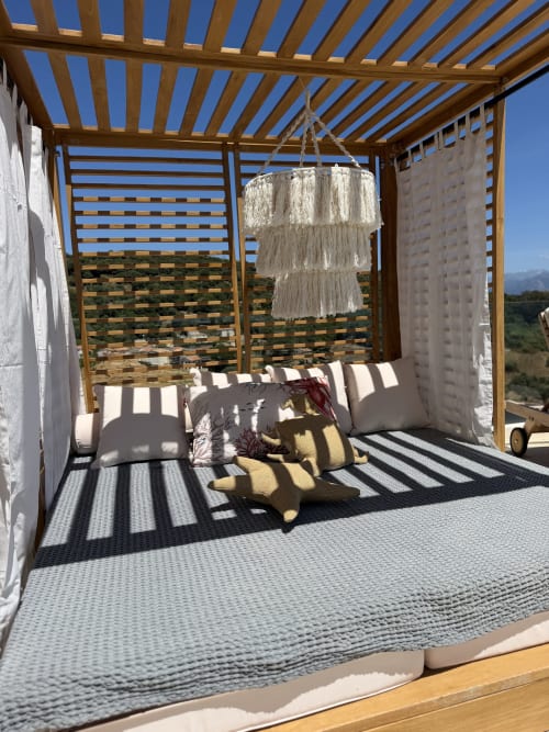 Pavillon de lit bohème en plein air au Petit Coin de Paradis avec coussins rayés, lustre macramé et vue sur la mer à Alata