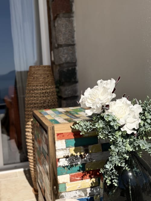 Orchidées blanches dans un pot noir avec verdure sur une table en bois colorée au Petit Coin de Paradis, Alata