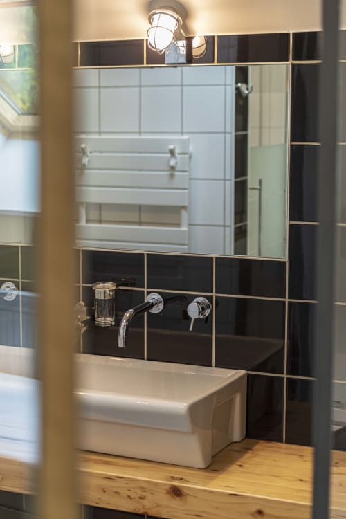 Lavabo moderne avec dosseret en carrelage noir et miroir au gîte Les Olivanies à Monthelon