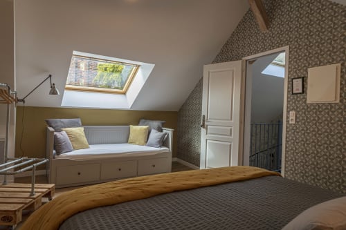 Chambre mansardée du gîte Les Olivanies à Monthelon avec lucarne, lit de repos et papier peint motifs