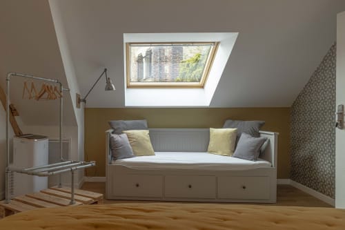 Chambre mansardée moderne avec puits de lumière, lit blanc avec rangements, mur accentué doré et vue sur la ville à la maison d'hôtes Les Olivanies, Monthelon