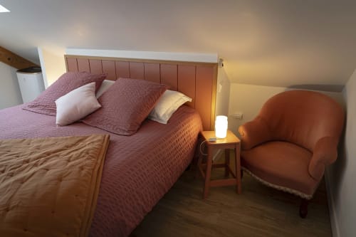 Chambre chaleureuse du gîte Les Olivanies à Monthelon avec literie bordeaux, tête de lit en bois et fauteuil d'accent