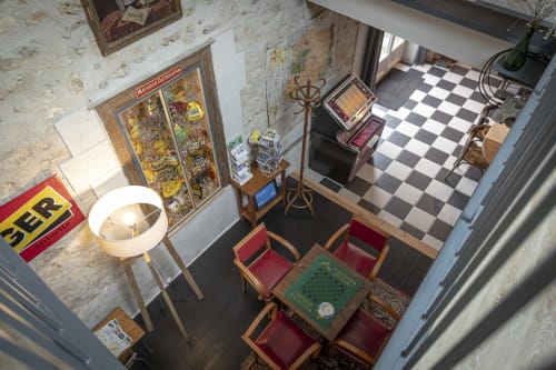 Vue aérienne du salon commun de la chaumière Les Olivanies avec table en damier, chaises rouges, décor vintage et carrelage à carreaux