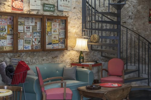 Salon vintage aux Olivanies : canapé bleu, fauteuils rouges, murs en pierre brute, affiches françaises anciennes
