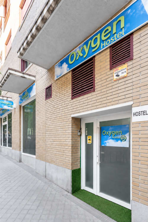 Entrada del Oxygen Hostel en Madrid con señalización azul, fachada de ladrillo y modernas puertas de cristal a nivel de calle