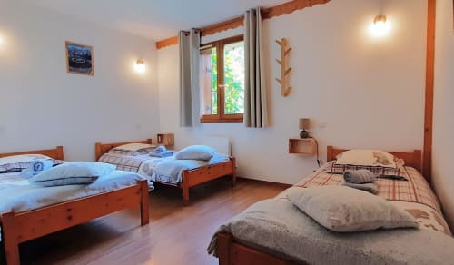 Chambre triple du Chalet De La Yodine avec lits en bois, vue sur le jardin et salle de bain privée
