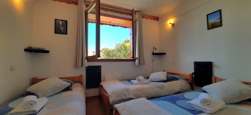 Chambre triple lumineuse au Chalet De La Yodine avec trois lits, mobilier en bois, vue montagne et ambiance chaleureuse
