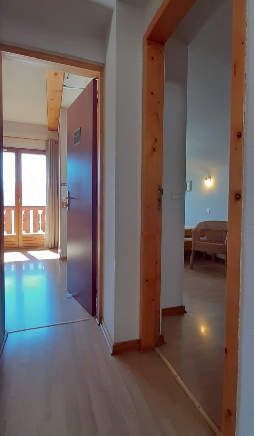 Couloir de chalet moderne avec poutres en bois, porte ouverte sur balcon et parquet clair au Chalet De La Yodine en Haute-Savoie