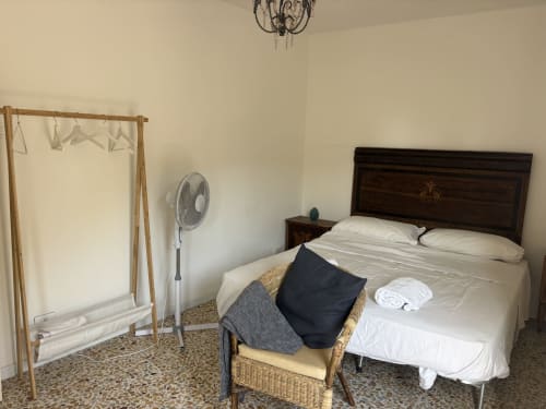 Camera da letto dell'appartamento Lovelyloft a Modica con letto, sedia in vimini, ventilatore e attaccapanni