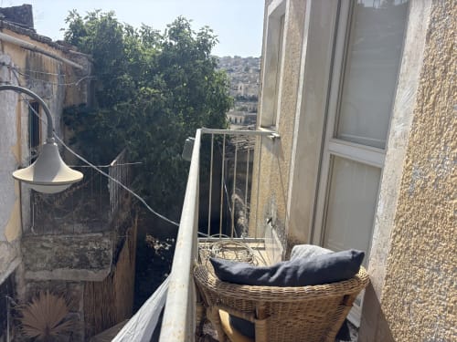 Terrazza del balcone di Lovelyloft a Modica con poltrona in vimini, vista sulla città e architettura siciliana tradizionale