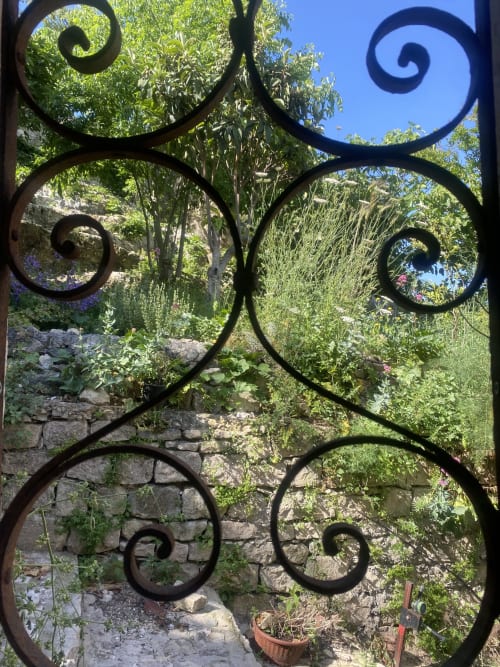 Elaborato cancello in ferro battuto che incornicia un lussureggiante giardino della villa Lovelyloft a Modica