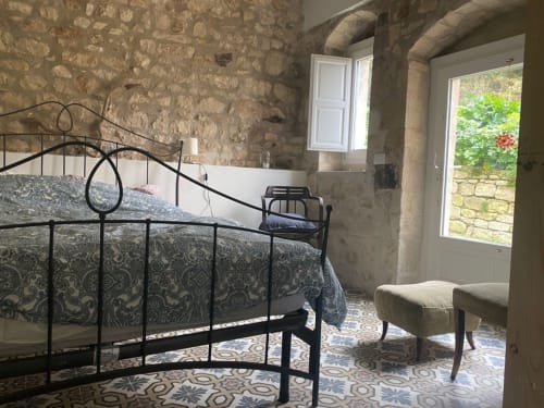 Camera in pietra rustica della villa Lovelyloft a Modica con letto in ferro battuto, biancheria decorata e porta con vista sul giardino