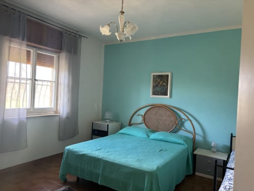 Camera da letto turchese con letto in rattan, finestra con vista sul mare, lampada a sospensione e opera d'arte presso la villa Lovelyloft a Scicli