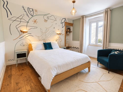 Chambre lumineuse aux Chambres D'Hespéris avec lit en bois, fresque murale, suspension et coin salon à Pleyben.