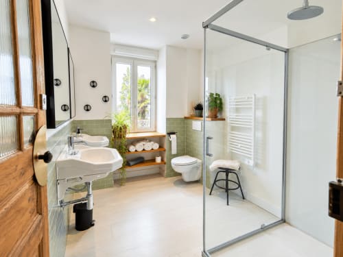 Salle de bain moderne aux Chambres D'Hespéris avec vasques doubles, carrelage vert, douche cascade et vue sur le jardin à Pleyben