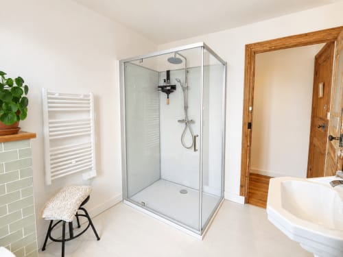 Salle de bain moderne avec cabine de douche vitrée, carrelage blanc et porte en bois aux Chambres D'Hespéris à Pleyben