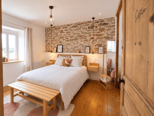 Chambre Solstice aux Chambres D'Hespéris à Pleyben, France, avec mur en pierre, lit en bois et luminaire suspendu