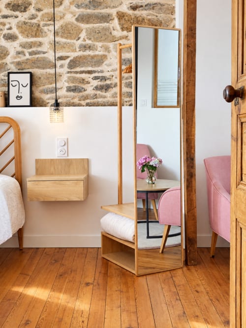 Chambre Solstice aux Chambres D'Hespéris à Pleyben : lit en bois, miroir, fauteuil rose et mur en pierre