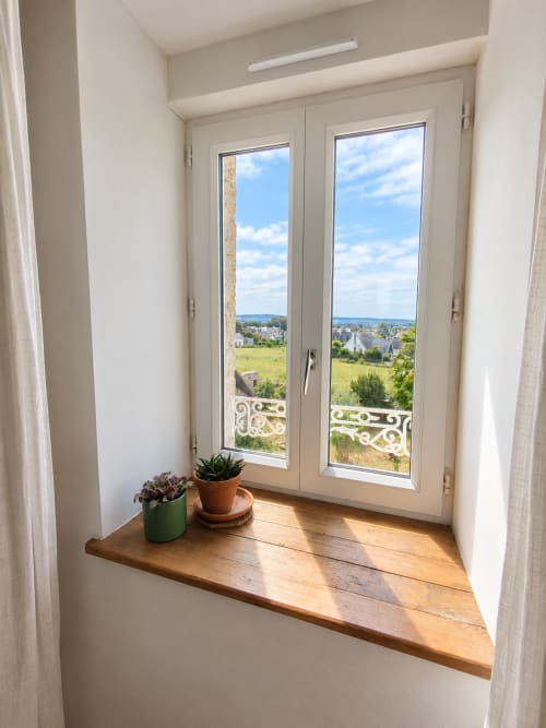 Vue de la campagne française depuis la chambre Solstice aux Chambres D'Hespéris, Pleyben, avec plantes en pot sur rebord de bois
