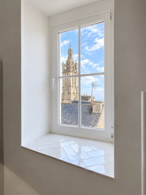 Fenêtre moderne de la chambre Pleyben surplombant le clocher historique et les toits d'ardoise sous un ciel bleu