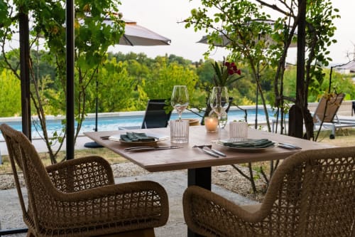 Outdoor dining setup at Domaine de la Peyrine with woven chairs, table settings, and pool view overlooking vineyard