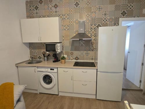 Cocina moderna en apartamento Brisalena Jerez Centro con armarios blancos, lavadora, estufa, refrigerador y diseño estampado
