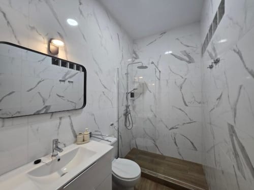 Baño moderno en apartamento Brisalena Jerez Centro con paredes efecto mármol, ducha abierta, lavabo, inodoro e iluminación empotrada
