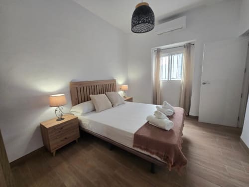 Dormitorio moderno en Brisalena Jerez Centro con cama de madera, lámparas de mesita, luz colgante y ventana en Jerez de la Frontera