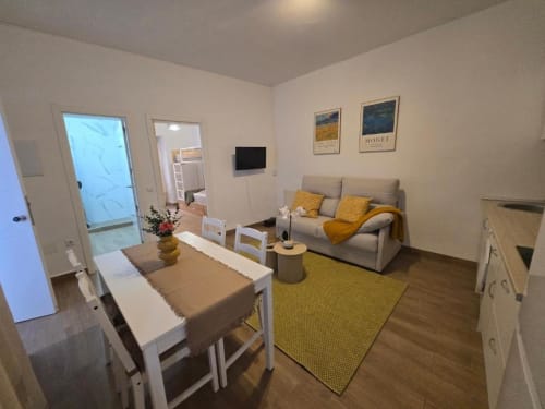 Sala moderna en Brisalena Jerez Centro con sofá gris, mesa de comedor, detalles amarillos y piso de madera