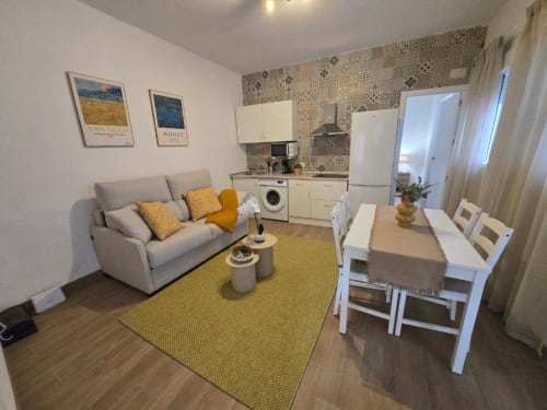 Luminoso apartamento de planta abierta en Jerez con sofá beige, toques amarillos, mesa de comedor, cocina equipada y diseño estampado