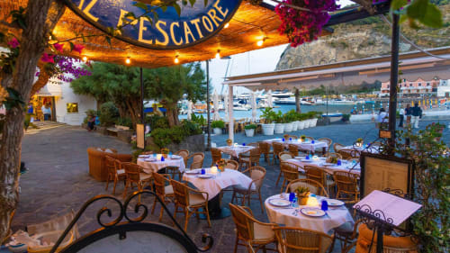 Terrazza con vista porto al Villa Bina Sea Hotel a Serrara Fontana: tavoli, sedie in vimini e panorama del porto al tramonto